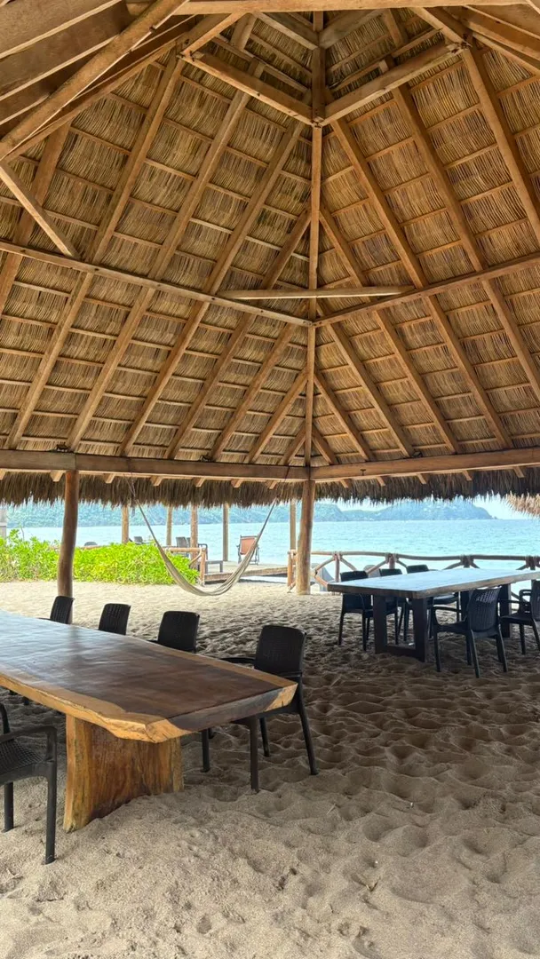 Mesas y hamaca bajo la palapa frente al mar